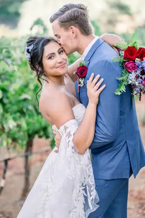 Groom kissing his bride on the cheek in a blue suit